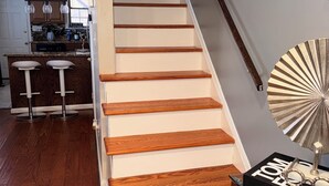 A staircase with wooden steps and a glass railing, leading to a landing with a kitchen area and a dining space.