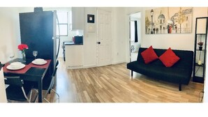 A modern living room with a black sofa and red cushions, a dining area with a table set for two, and a hallway leading to a door. - Stylish 1 Brm Apartment in the Heart of Miami! #9 (Miami)