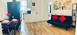 A modern living room with a black sofa and red cushions, a dining area with a table set for two, and a hallway leading to a door. - Stylish 1 Brm Apartment in the Heart of Miami! #9 (Miami)