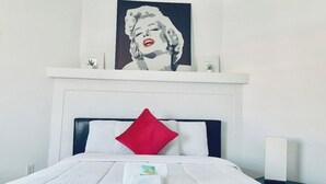 A hotel room with a bed, a red pillow, a white blanket, a framed artwork above the bed, and a nightstand with a lamp. - Stylish 1 Brm Apartment in the Heart of Miami! #9 (Miami)