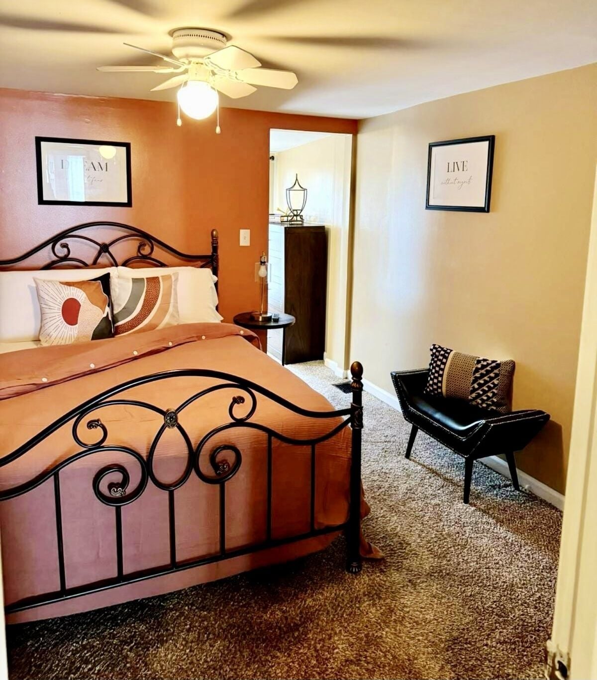 A bedroom with a bed, a chair, a ceiling fan, and two framed pictures on the wall.