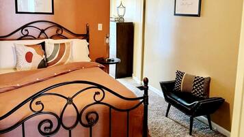 A bedroom with a bed, a chair, a ceiling fan, and two framed pictures on the wall.