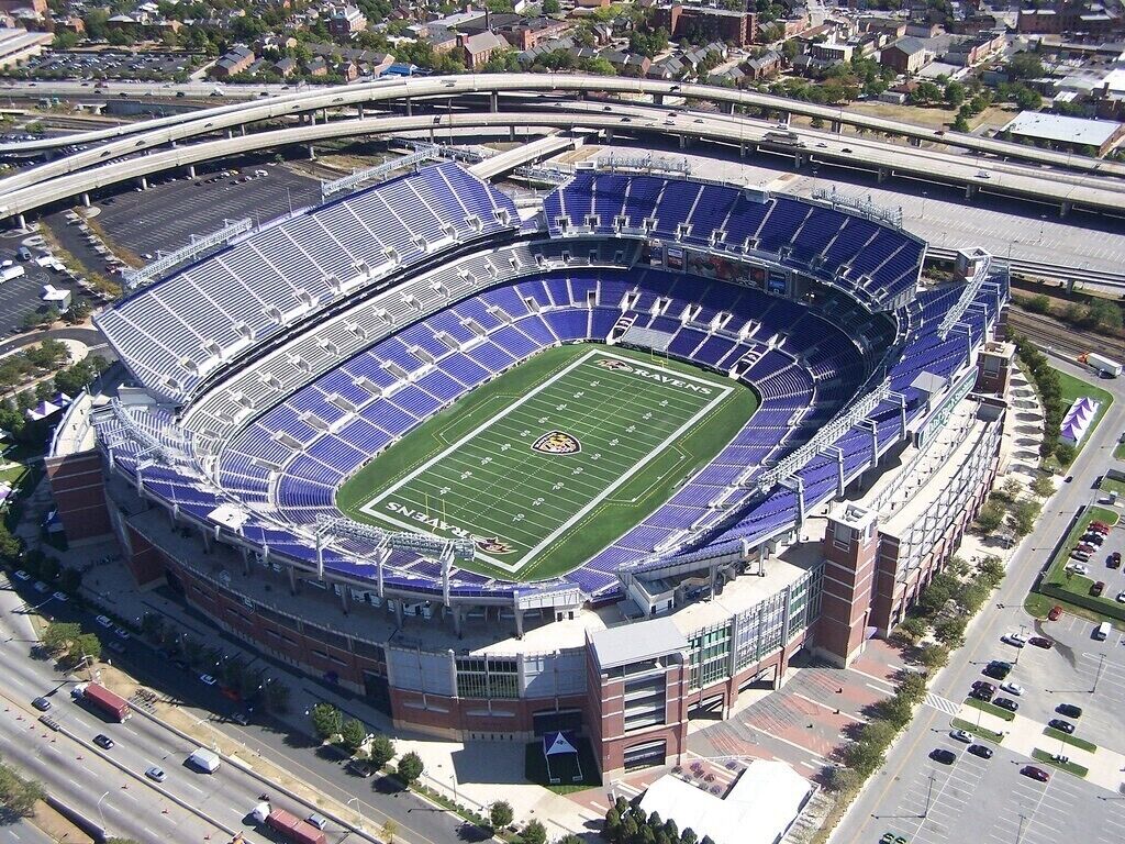 A stadium with a football field, seating areas, and a parking lot.