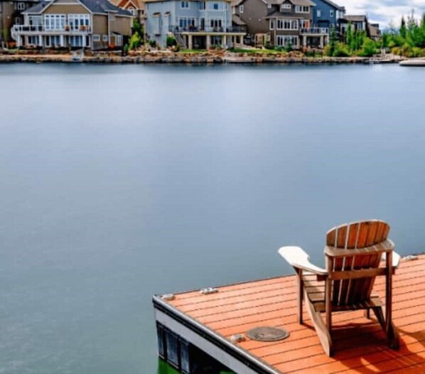 Ein Wohnhaus am Wasser mit einer Holzterrasse und einem einzelnen Adirondack-Sessel.