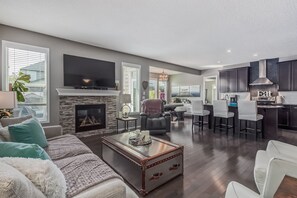 Ein geräumiges Wohnzimmer mit Kamin, Fernseher und Küchenbereich mit dunklen Schränken und einer Bar.