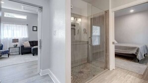 Une chambre à coucher moderne avec une cabine de douche en verre, un lit recouvert d’une couverture grise et une petite table de chevet.