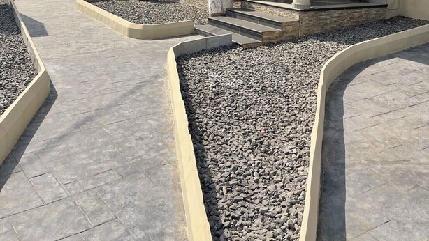 Um edifício moderno com um pátio coberto, colunas de pedra e um caminho de cascalho.