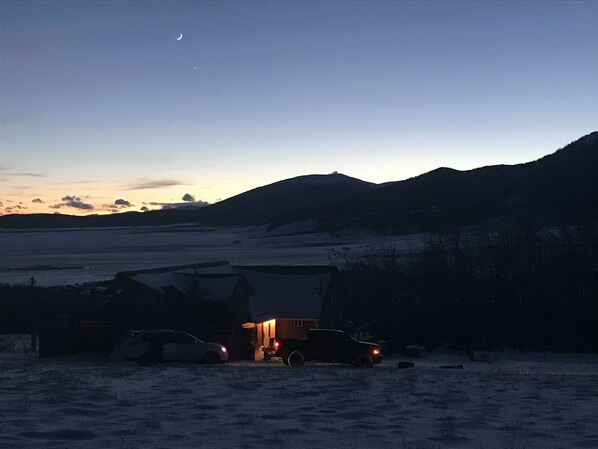 A snowy landscape with a building and parked cars at dusk.