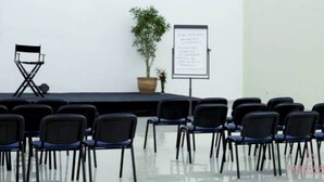 Un salón de conferencias con escenario, sillas, una pizarra y una planta en maceta.