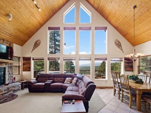 A spacious living area with a large sectional sofa, a dining table with chairs, and a fireplace. - Valley View Cabin, New Hot Tub, Close to Ski Lifts! (Angel Fire)