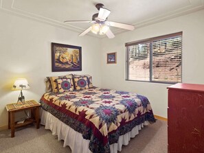 A bedroom with a bed, a ceiling fan, a window with blinds, a nightstand with a lamp, and a red dresser. - Valley View Cabin, New Hot Tub, Close to Ski Lifts! (Angel Fire)