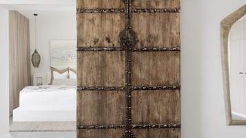 A rustic wooden sliding door with metal studs, a bed with white bedding, a hanging light fixture, and a partial view of a room with a white wall and a wooden archway.