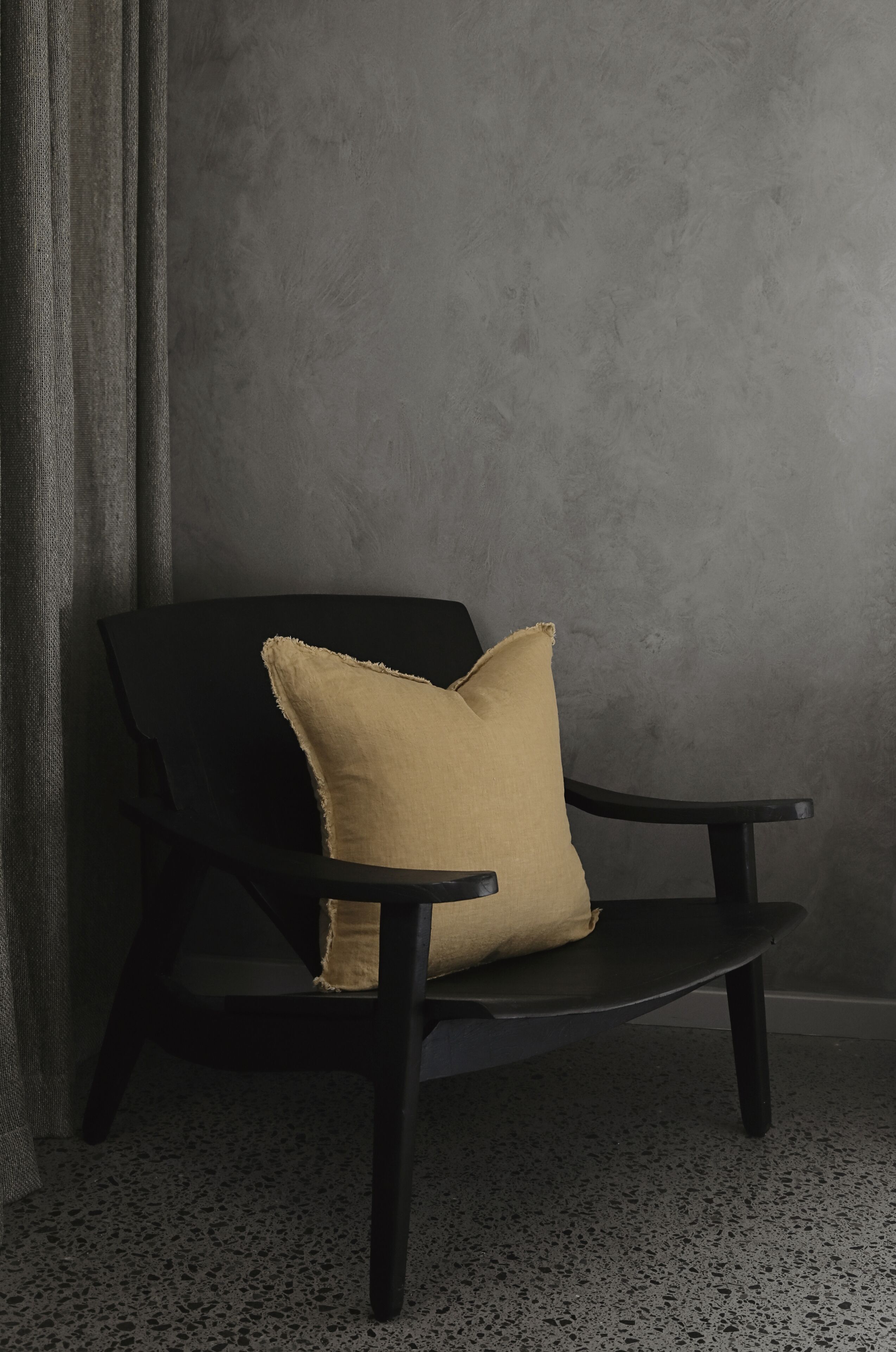 A black chair with a beige cushion against a textured grey wall.