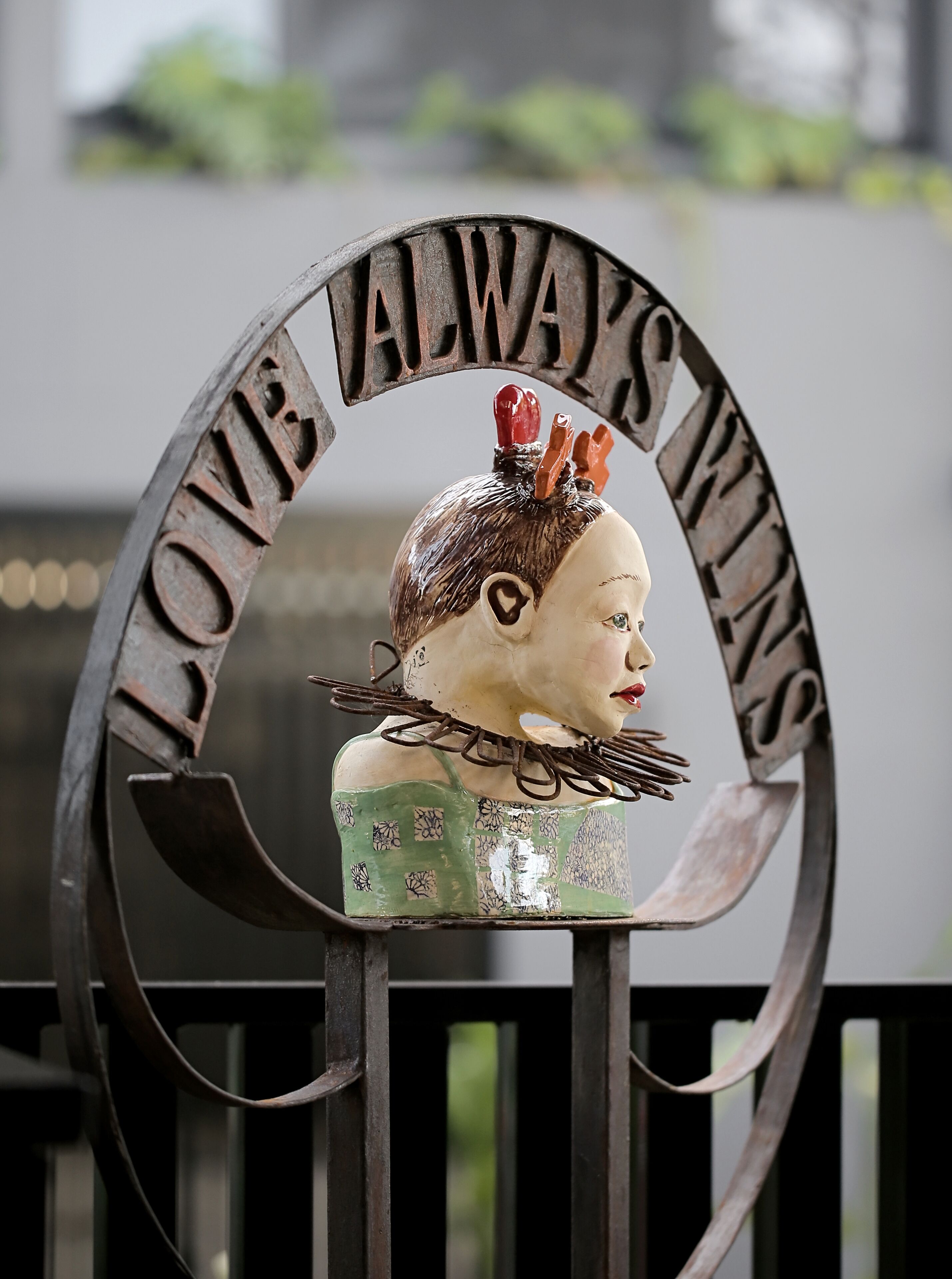 A decorative metal sign with the inscription "LOVE ALWAYS WINS" and a sculpted bust.