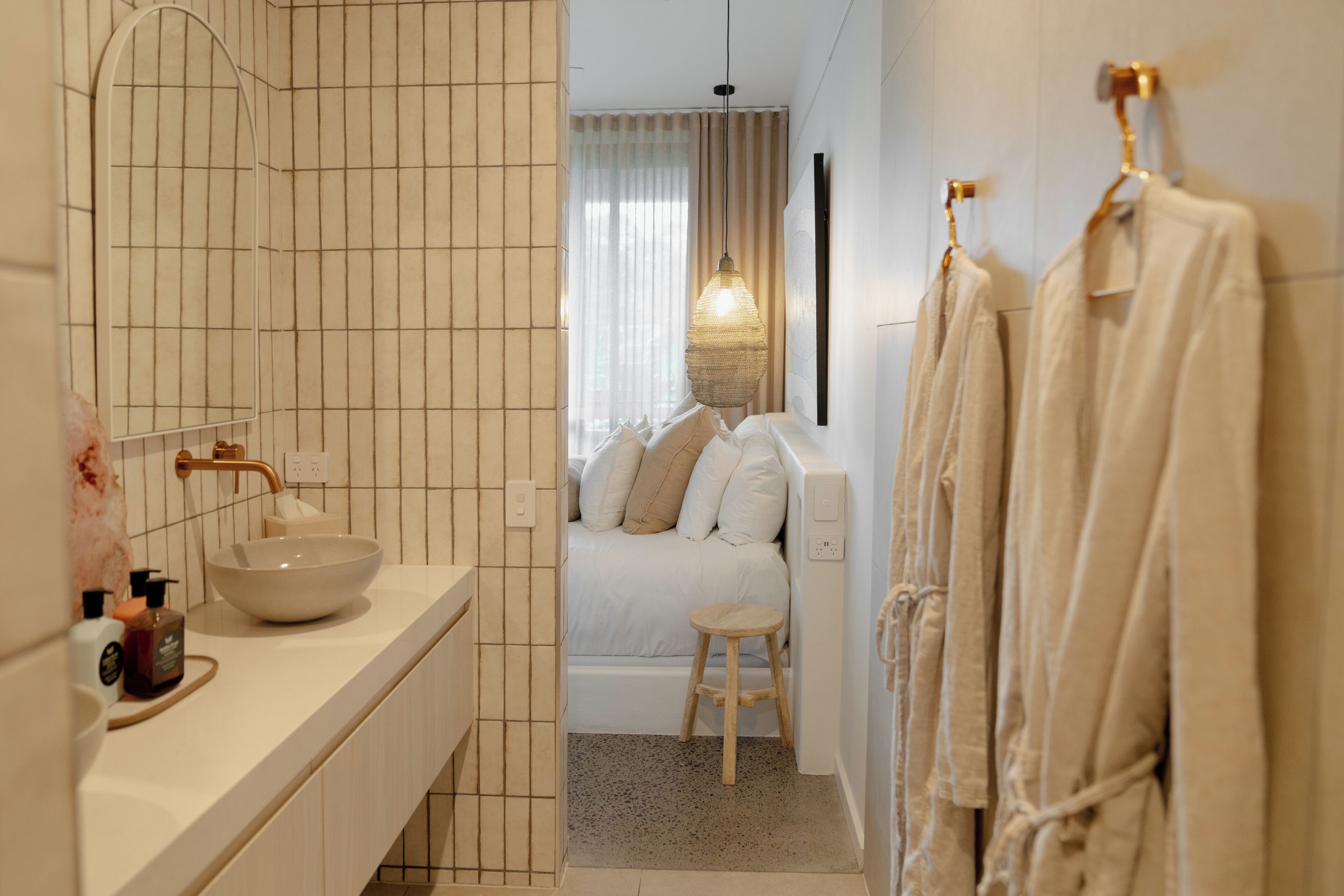 A modern bathroom with a large mirror, a bowl sink, a bathtub, and a wooden stool.