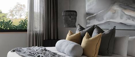 A modern bedroom with a large bed, a view of greenery outside, and a unique wall art piece.