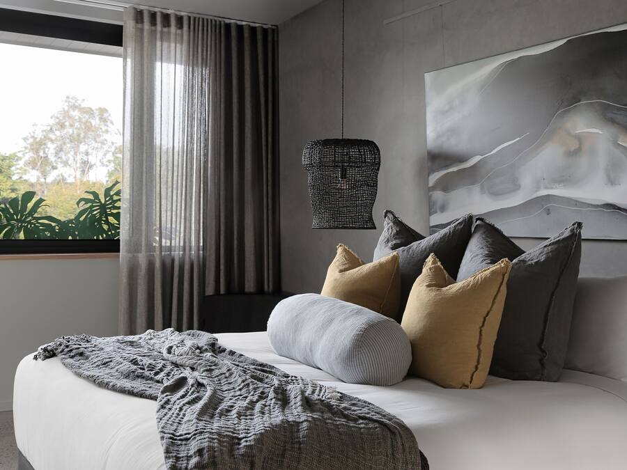 A modern bedroom with a large bed, a view of greenery outside, and a unique wall art piece.