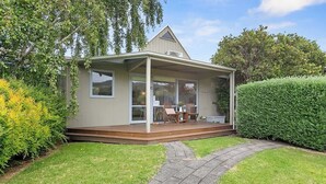 A single-story house with a covered porch, a small patio with outdoor furniture, and a well-maintained lawn. - Bay Beach Hut ~ Heated Floor ~ 50m Cafes (Apollo Bay)
