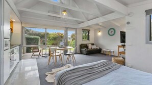A spacious bedroom with a large bed, a dining area with chairs, a sofa, and a TV. - Bay Beach Hut ~ Heated Floor ~ 50m Cafes (Apollo Bay)