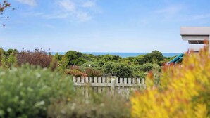A view of a coastal area with a wooden fence, greenery, and a building with a blue roof. - Bay Beach Hut ~ Heated Floor ~ 50m Cafes (Apollo Bay)
