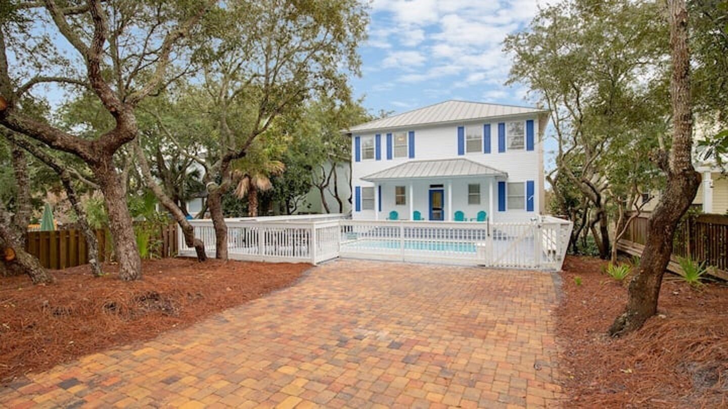 A two-story house with a front porch, a swimming pool, and a brick driveway.