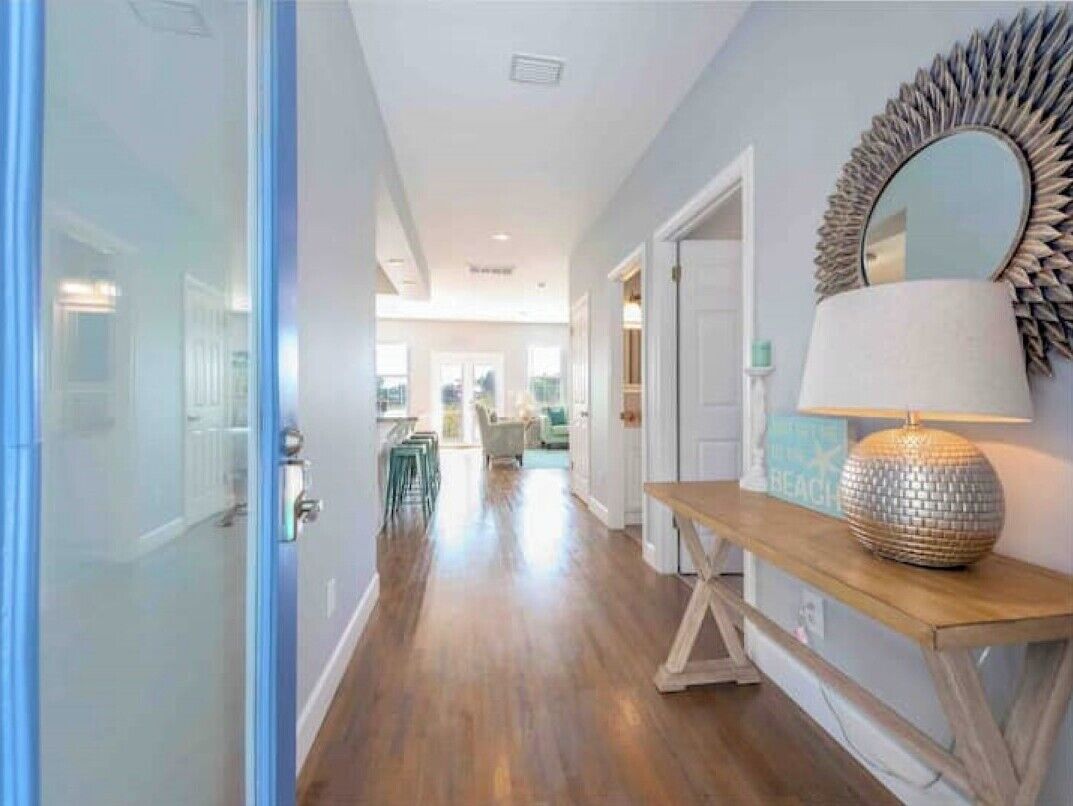 A hallway with wooden flooring, a bench, a decorative mirror, and a door leading to another room.