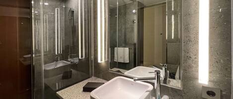 Un baño moderno con ducha de vidrio, un lavabo amplio y un espejo.