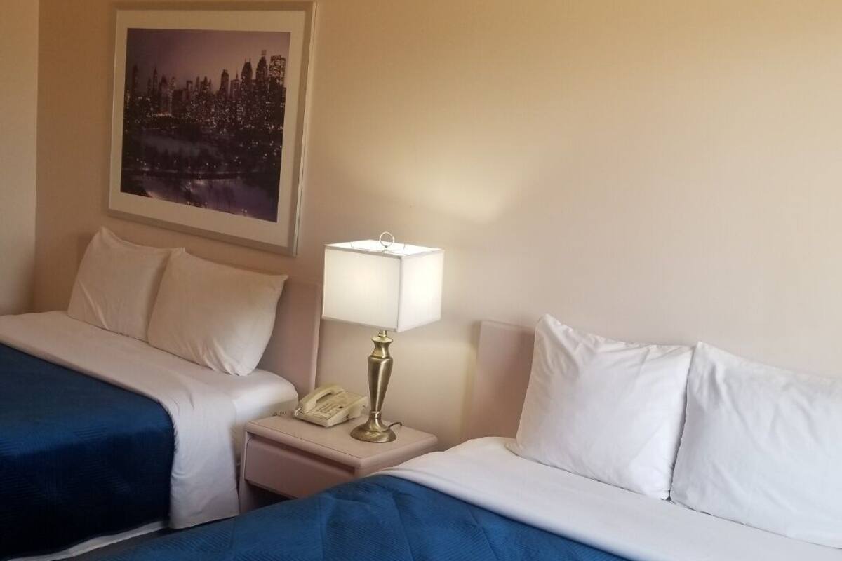 Habitación de hotel con dos camas, una mesita de noche, una lámpara, un teléfono y un cuadro en la pared.