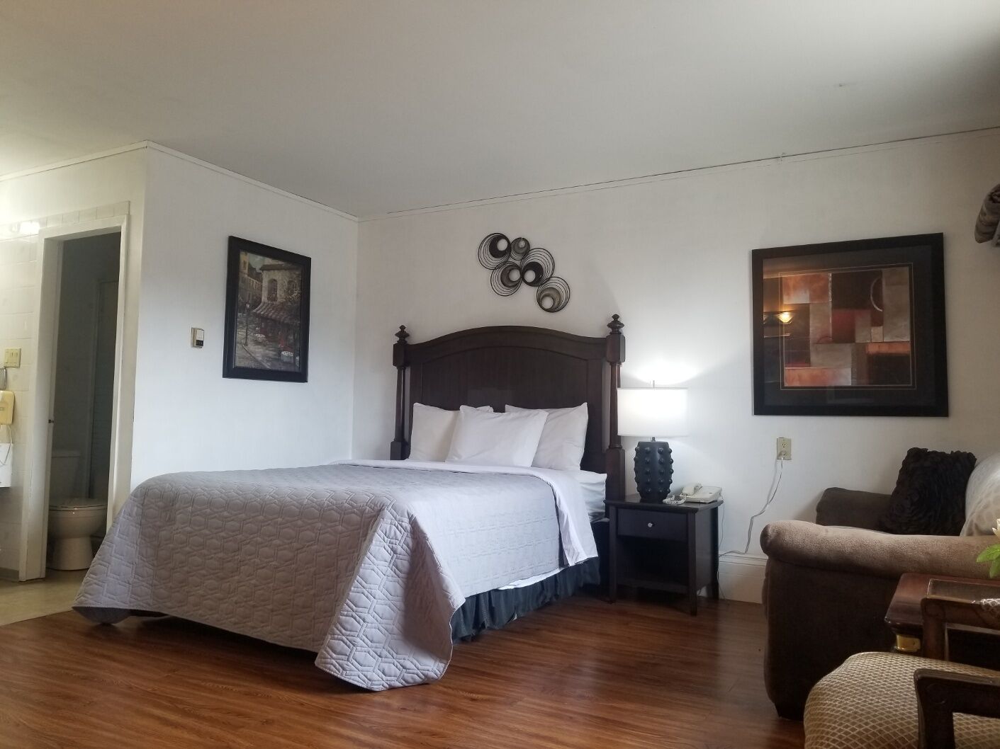 Un dormitorio con una cama grande, una mesita de noche, una silla y una obra de arte en la pared.