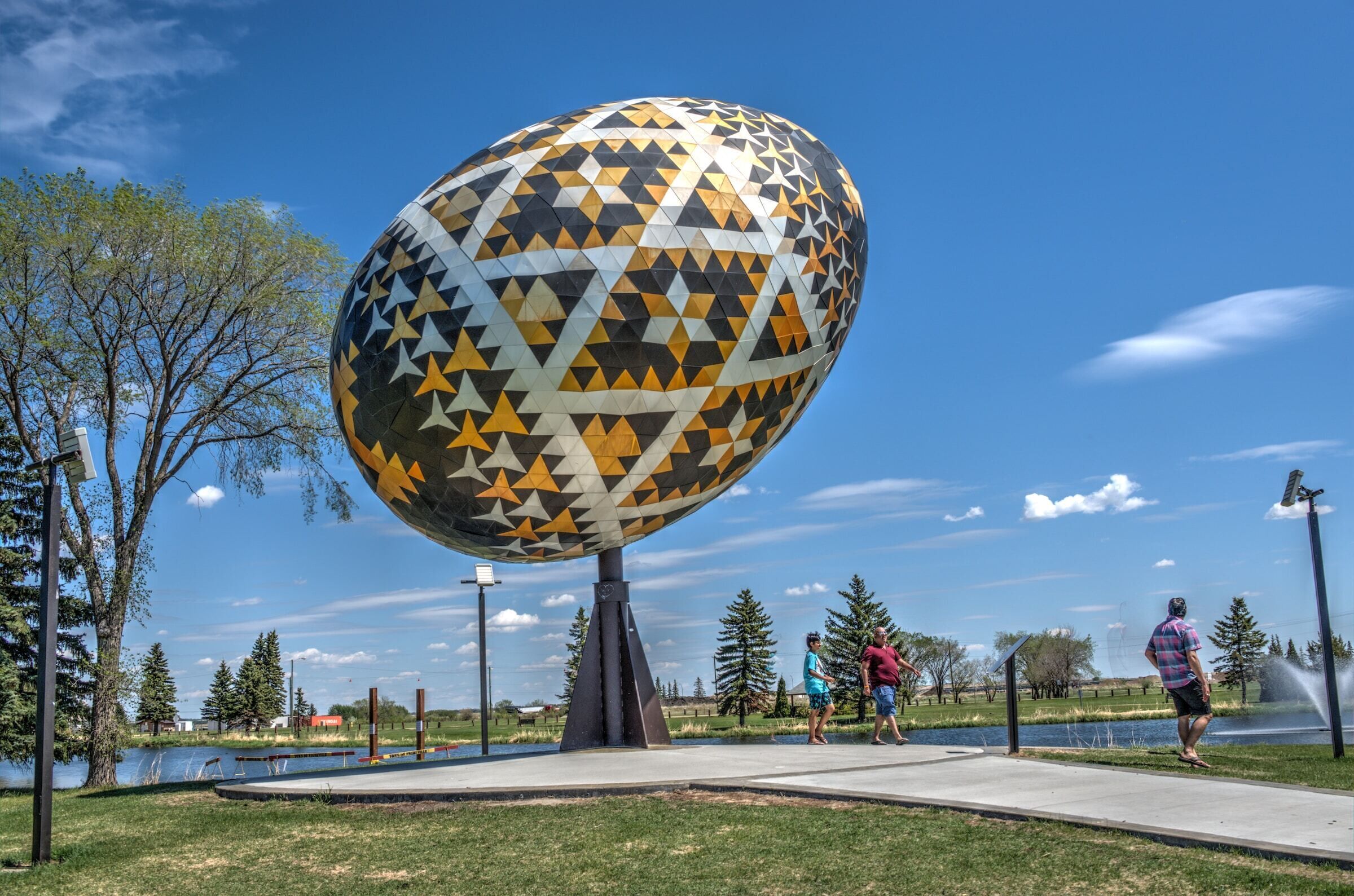 Une sculpture sphérique ornée d’un motif géométrique, située dans un parc.
