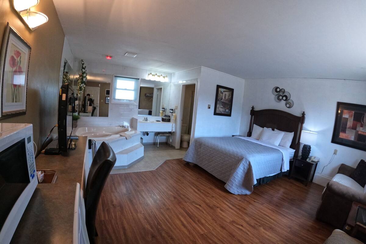 Habitación de hotel con una cama grande, un escritorio, una silla, un microondas y un baño con bañera.