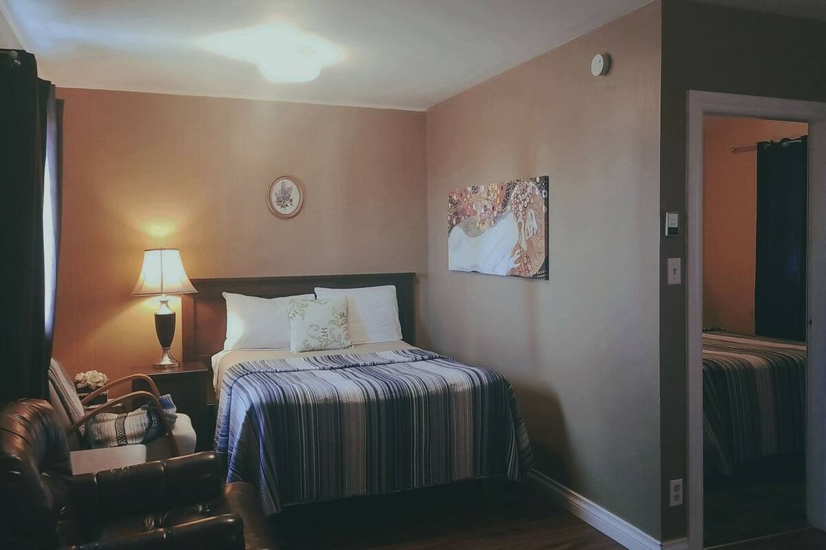 Una habitación de hotel con una cama, una mesita de noche, una lámpara, una silla y un cuadro en la pared.