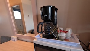 Un horno microondas con una cafetera encima, un vaso de agua y una taza de café sobre la encimera.
