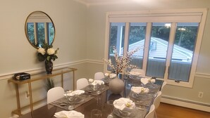Een eetkamer met een tafel met glazen blad, gedekt voor vier personen, witte stoelen, een vaas met bloemen en een spiegel aan de muur.