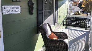 A porch with a wicker chair, a bench, a decorative sign, and a lantern.
