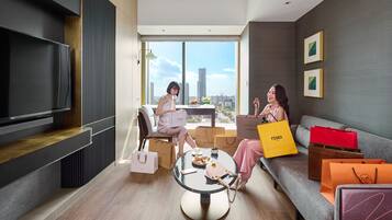 Una sala de estar moderna con un televisor grande, un comedor con mesa y sillas, y un sofá con bolsas de compras.
