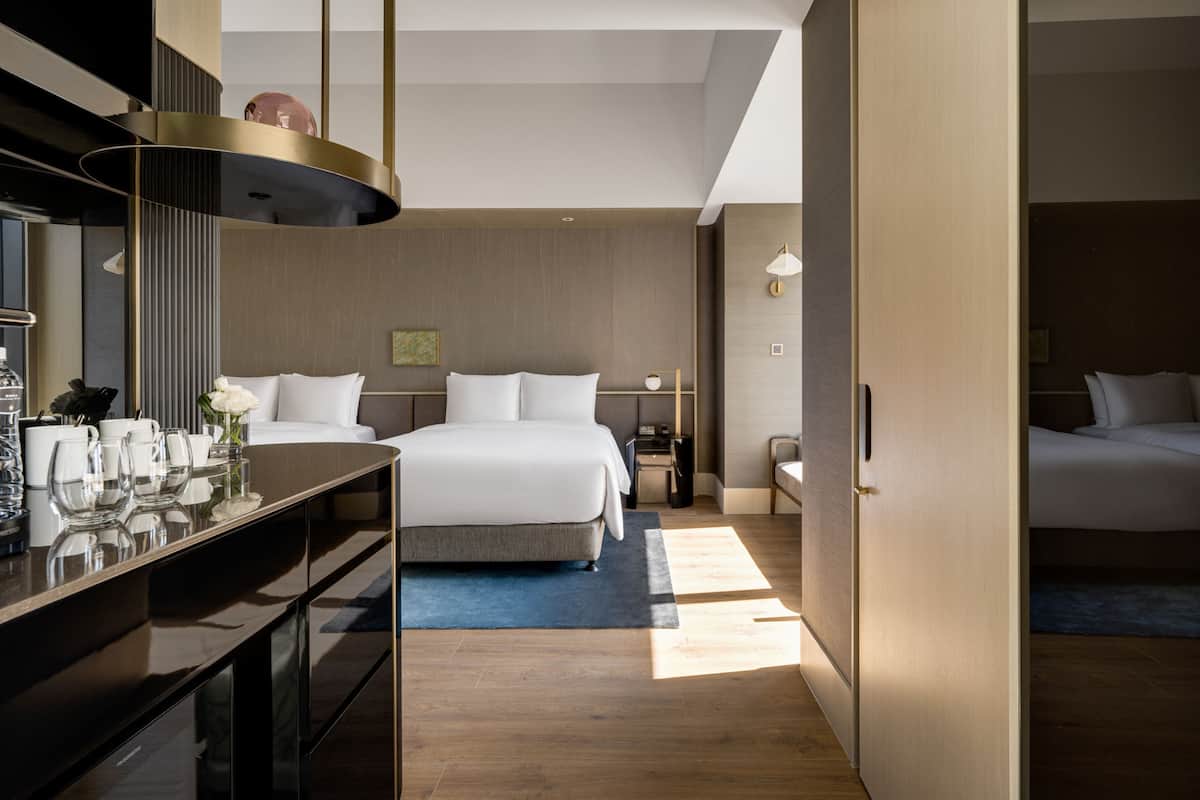 Ein modernes Hotelzimmer mit einem großen Bett, einem Schreibtisch mit Lampe und Blick auf den Flur.