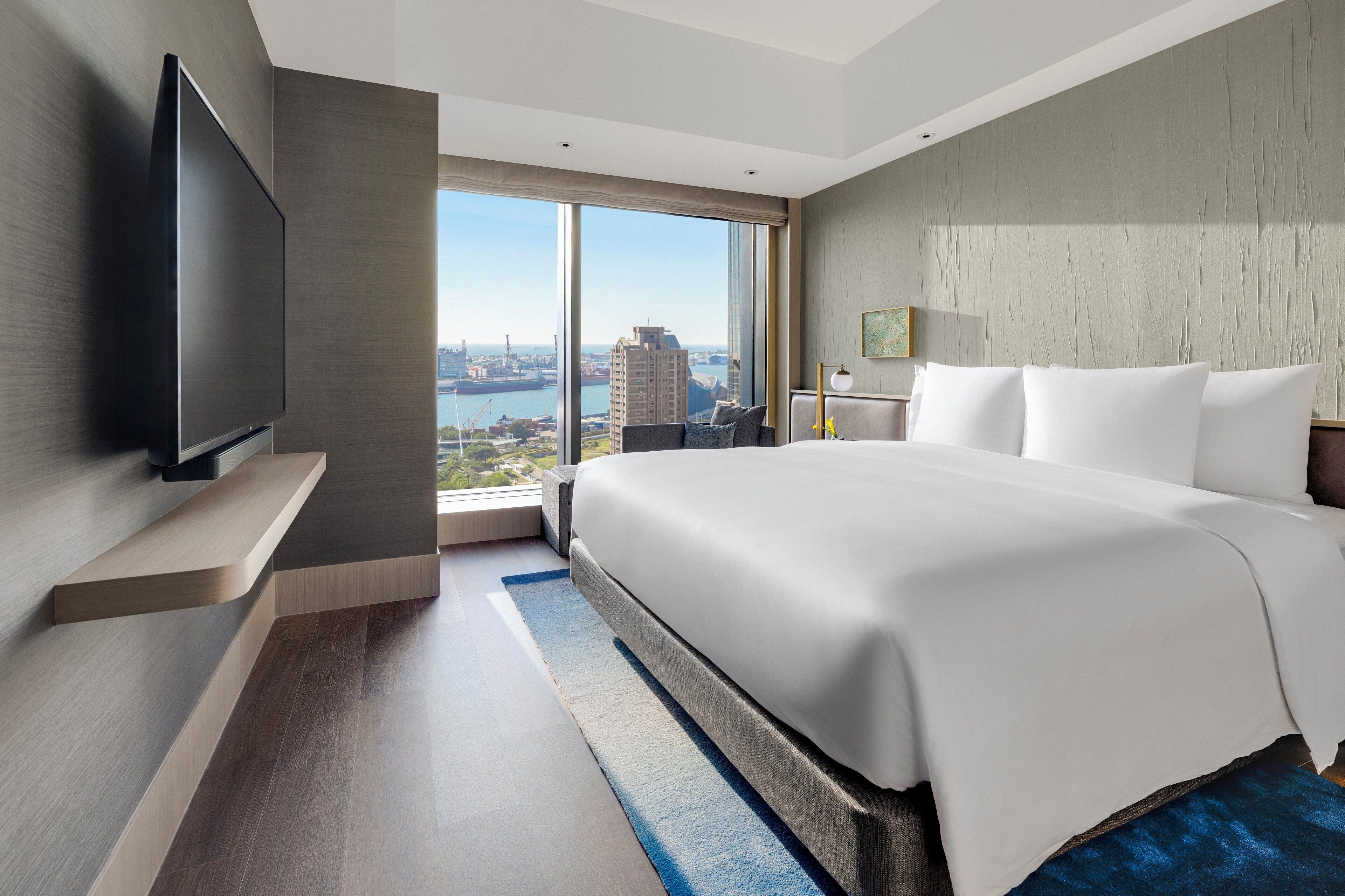 A modern hotel room with a large bed, a flat-screen TV, and a city view.