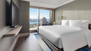 A modern hotel room with a large bed, a flat-screen TV, and a city view.
