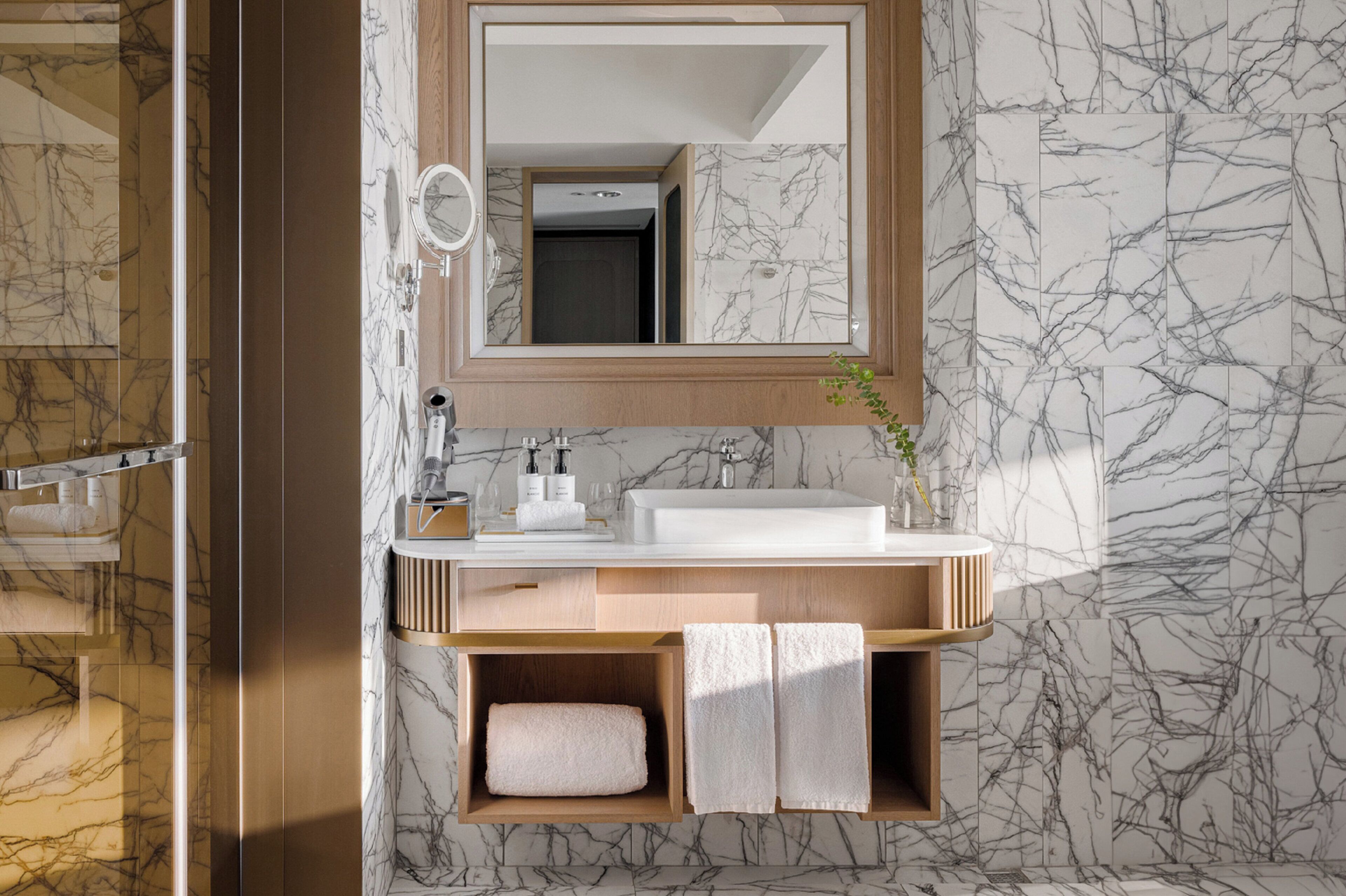 A bathroom with a marble wall, a wooden vanity, a mirror, a sink, and a towel rack.