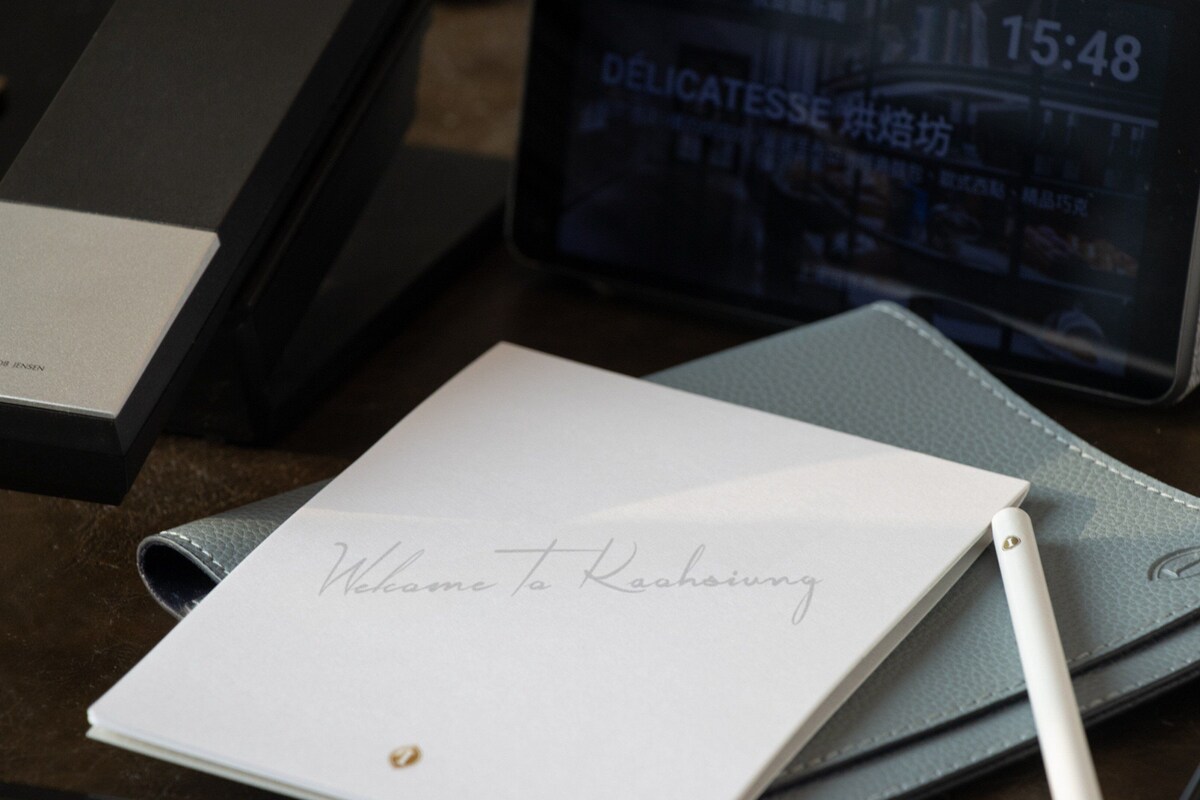 A notebook with a handwritten note, a pen, a digital clock, and a black box with 'JACOB JENSEN' on it.
