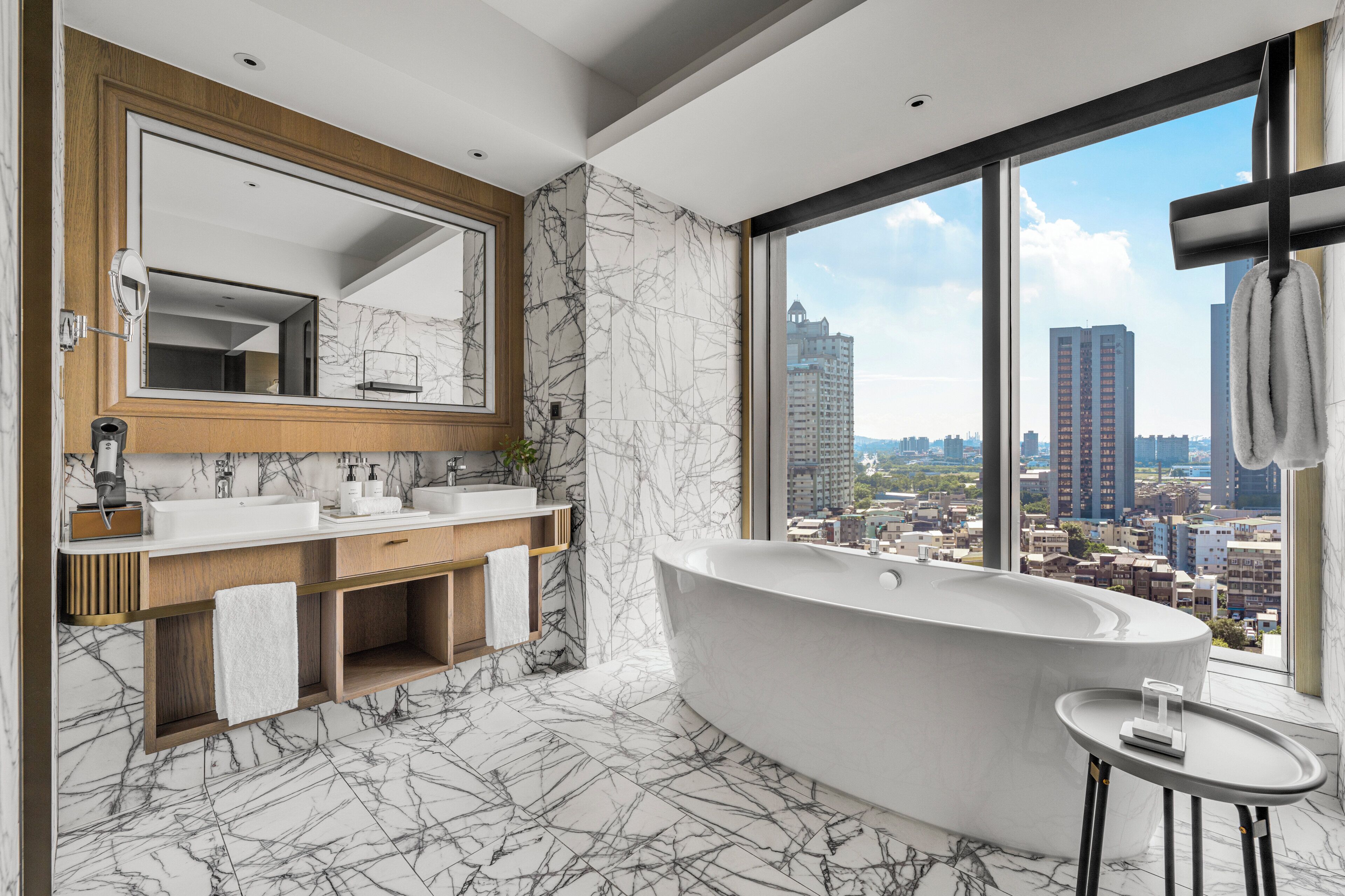 A modern bathroom with a freestanding bathtub, a large mirror, and a view of a cityscape through large windows.