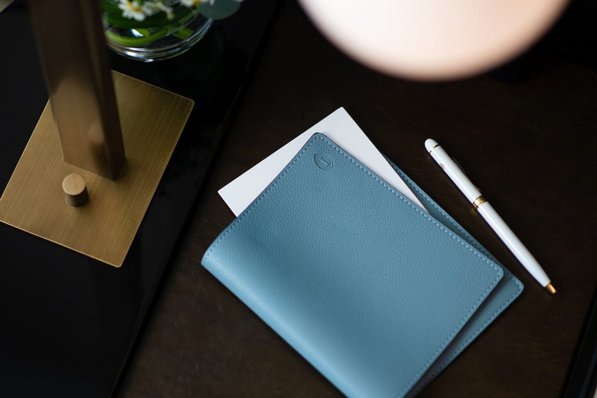 Ein runder Tisch mit schwarzer Tischplatte, einem blauen Notizbuch, einem weißen Stift und einem kleinen Glasgefäß mit einer Blume.