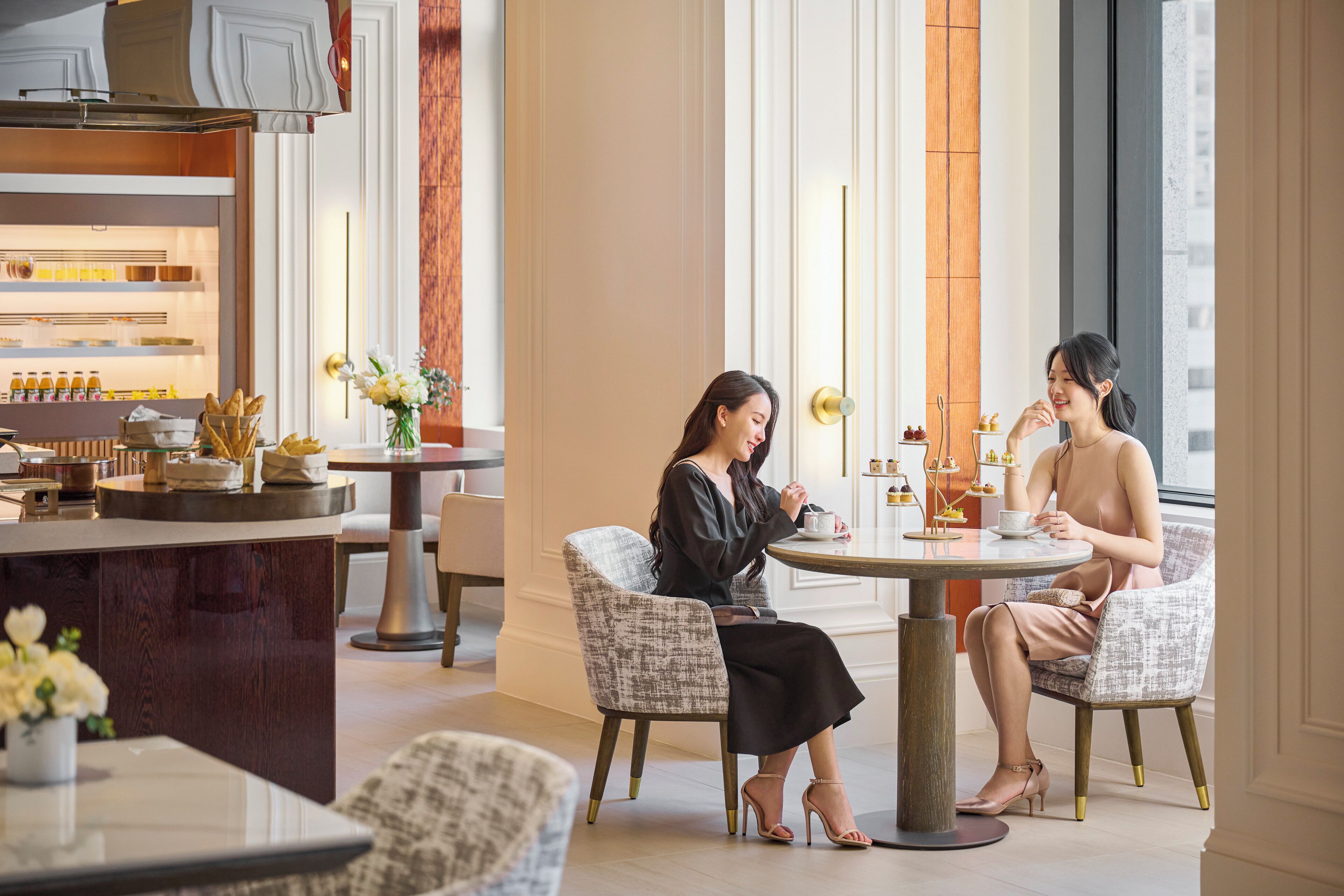 A modern interior with two people seated at a round table, surrounded by elegant furnishings and a well-lit space with large windows.