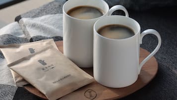 Two white coffee cups on a wooden coaster, a brown paper bag with text, and a grey couch.