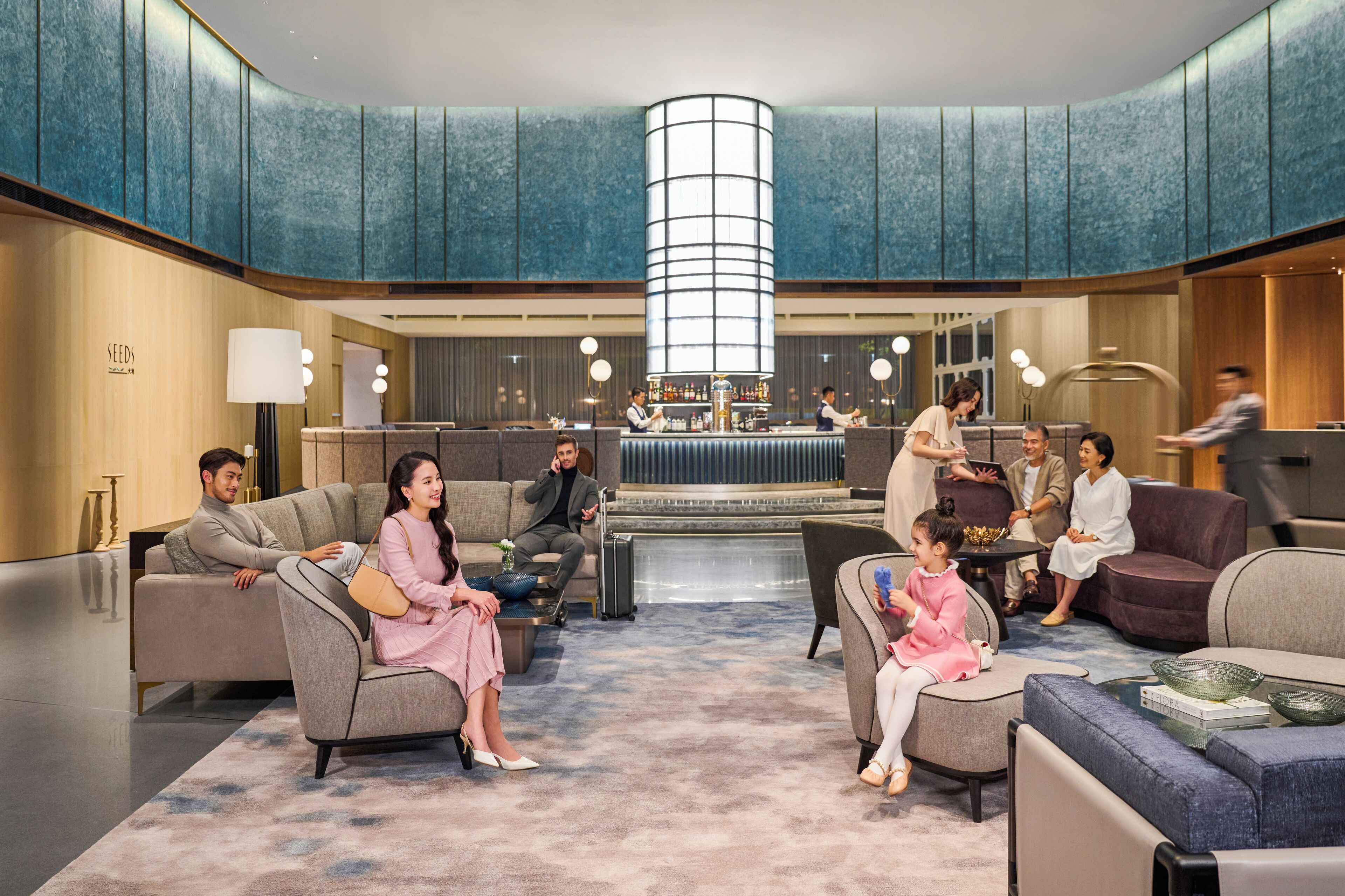 A spacious lobby with seating areas, a bar, and a central light fixture.