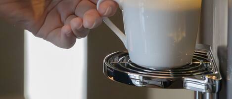 En hånd holder en hvid kop under en kaffemaskine, mens kaffe fyldes i koppen.