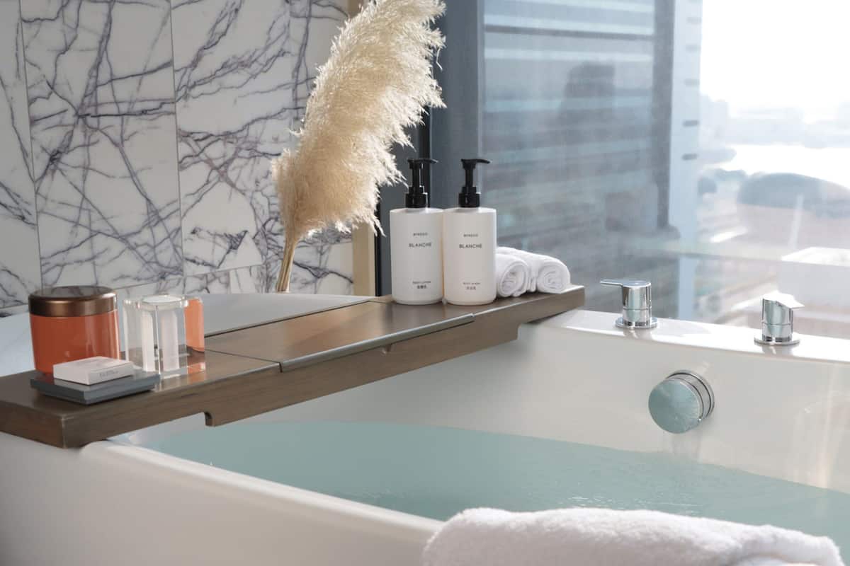 Ein modernes Badezimmer mit Marmorwand, einer Badewanne mit Ausblick und Pflegeprodukten auf einem Regal.