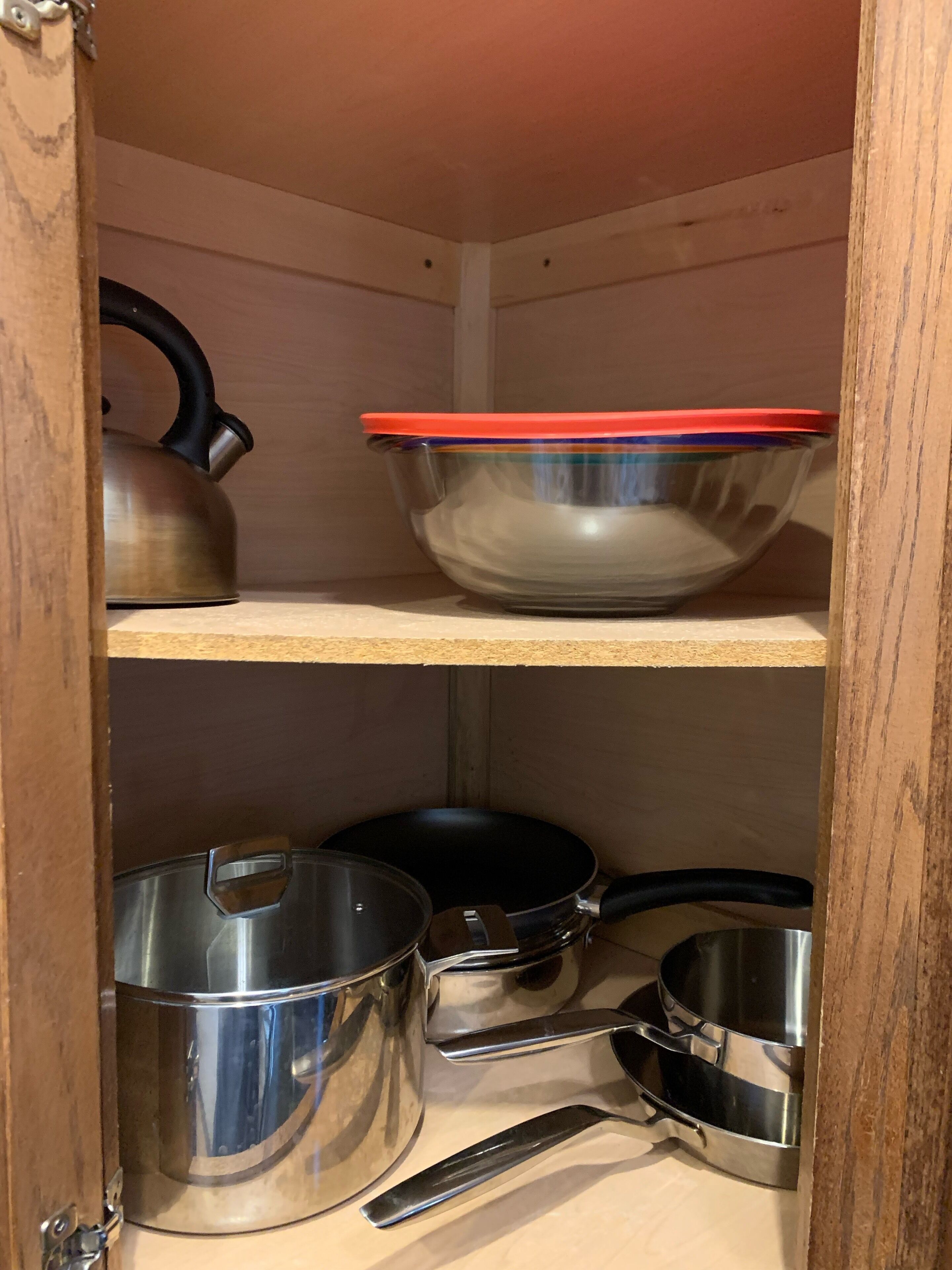 Een houten kast met planken vol keukengerei, zoals een waterkoker, een kom en verschillende pannen.