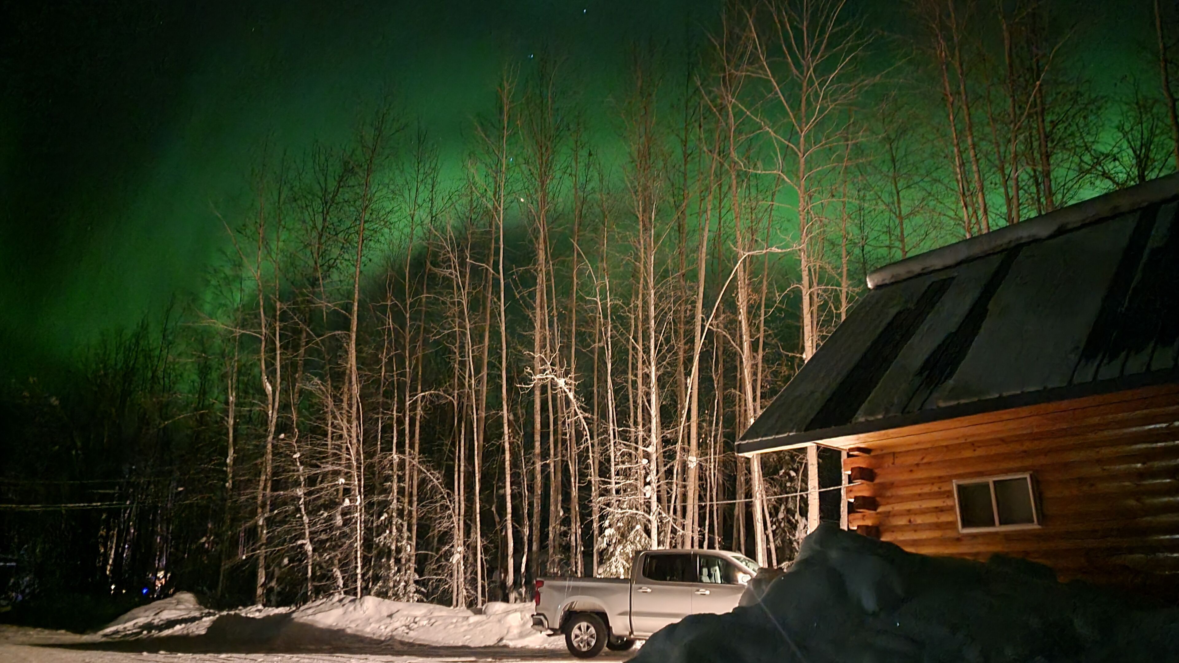A cabin with a truck parked in front, surrounded by a forest.
